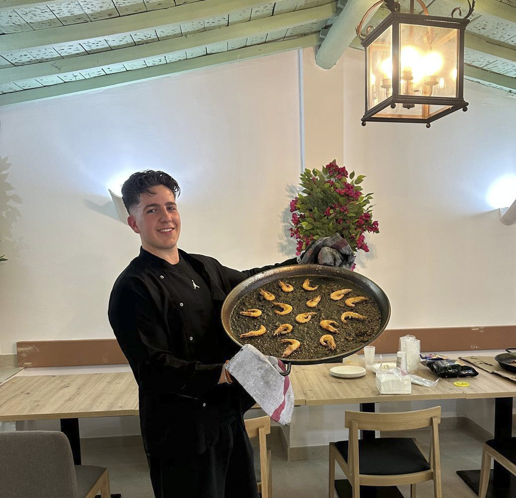 Benji, chef del Restaurante Los Pinochos en Simancas (Valladolid), con una paella en la mano bajo la luz de un farol del comedor